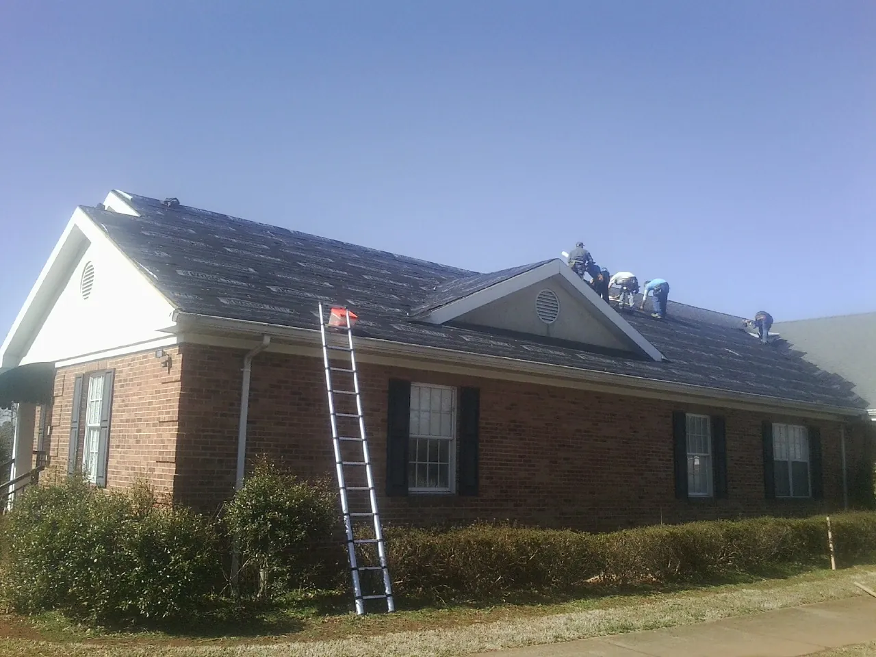 Crew tearing shingles off a brick ranch roof with a ladder set — Emergency Roof Repair work by our crew in Mill Hall