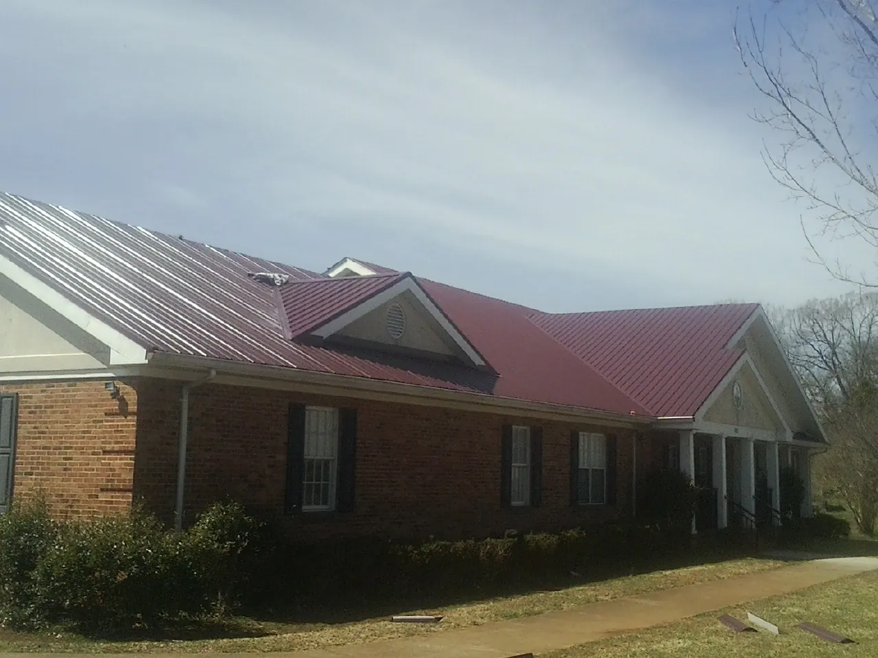 Red metal roof with gabled entries on a long brick building, from a Hail Damage Roof Repair job in Mill Hall