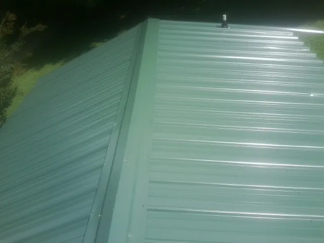 New green metal panels meeting at the ridge of a roof — Flat Roof Repair work by our crew in Mill Hall
