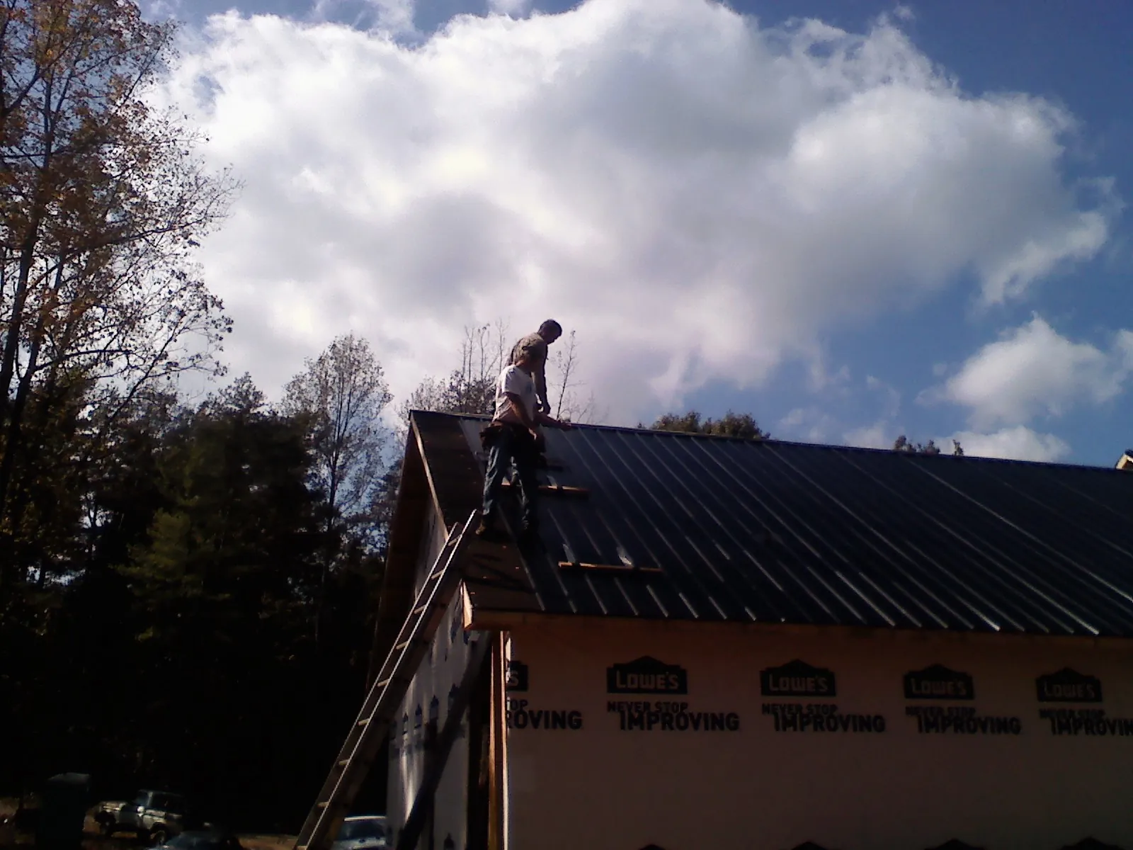 Roofer fastening dark metal panels high against a cloudy sky, from a Roof Inspection job in Mill Hall