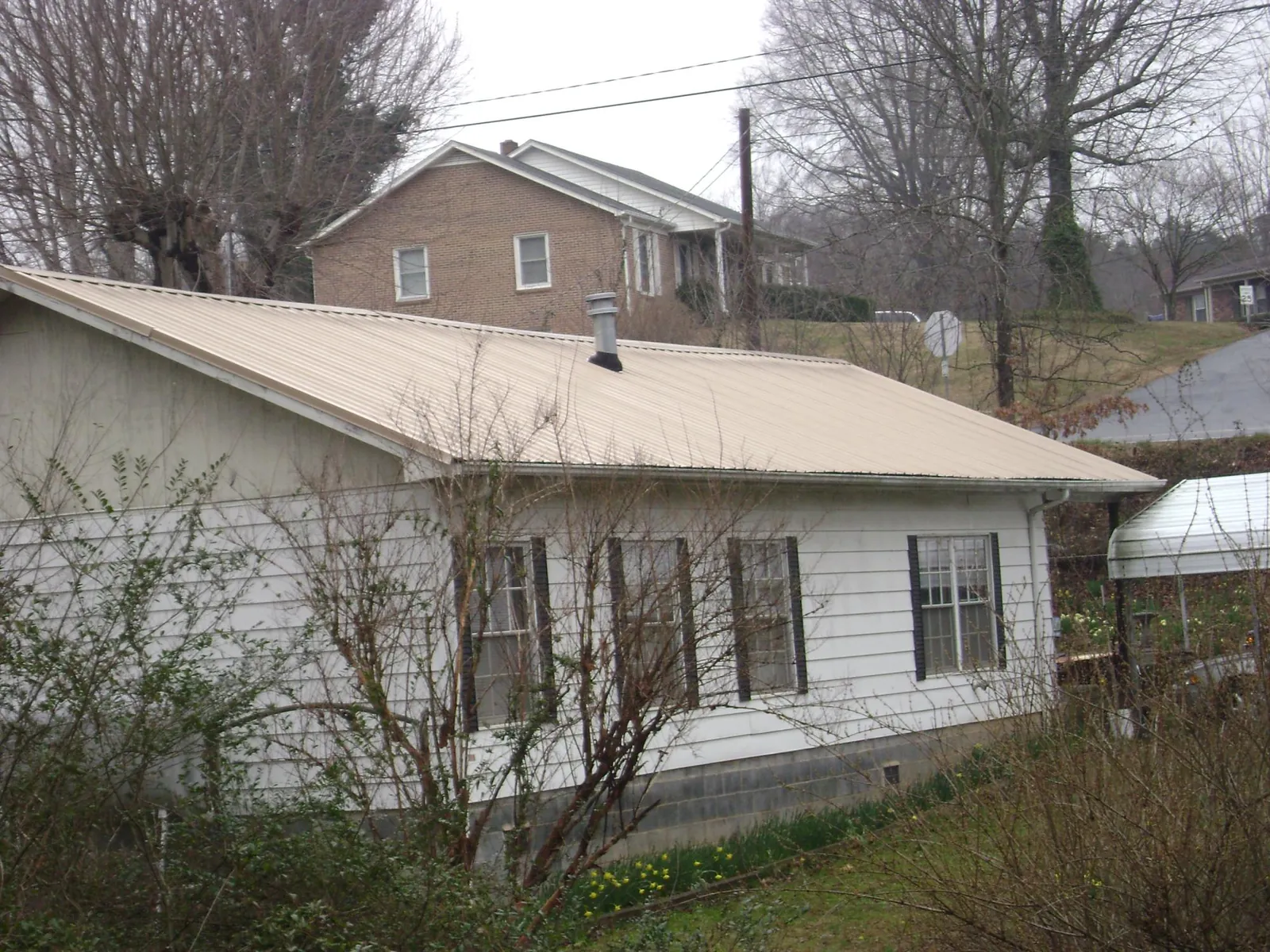 Tan metal roof on a white sided house set into a hillside — Commercial Roofing by Roofing Brothers in Mill Hall