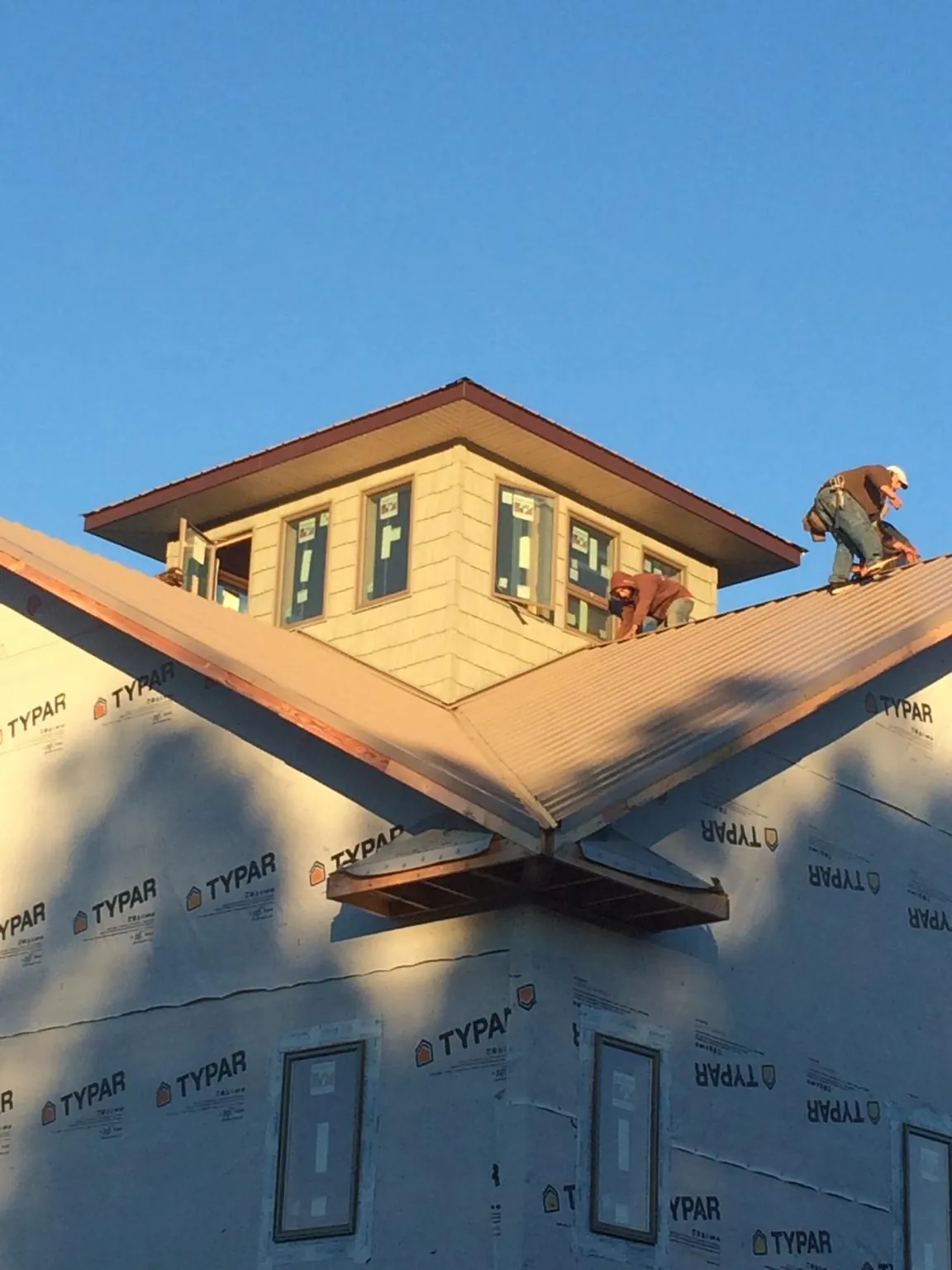 Roofers working around a rooftop cupola on a new metal roof at sunset — Roof Waterproofing in Mill Hall by Roofing Brothers